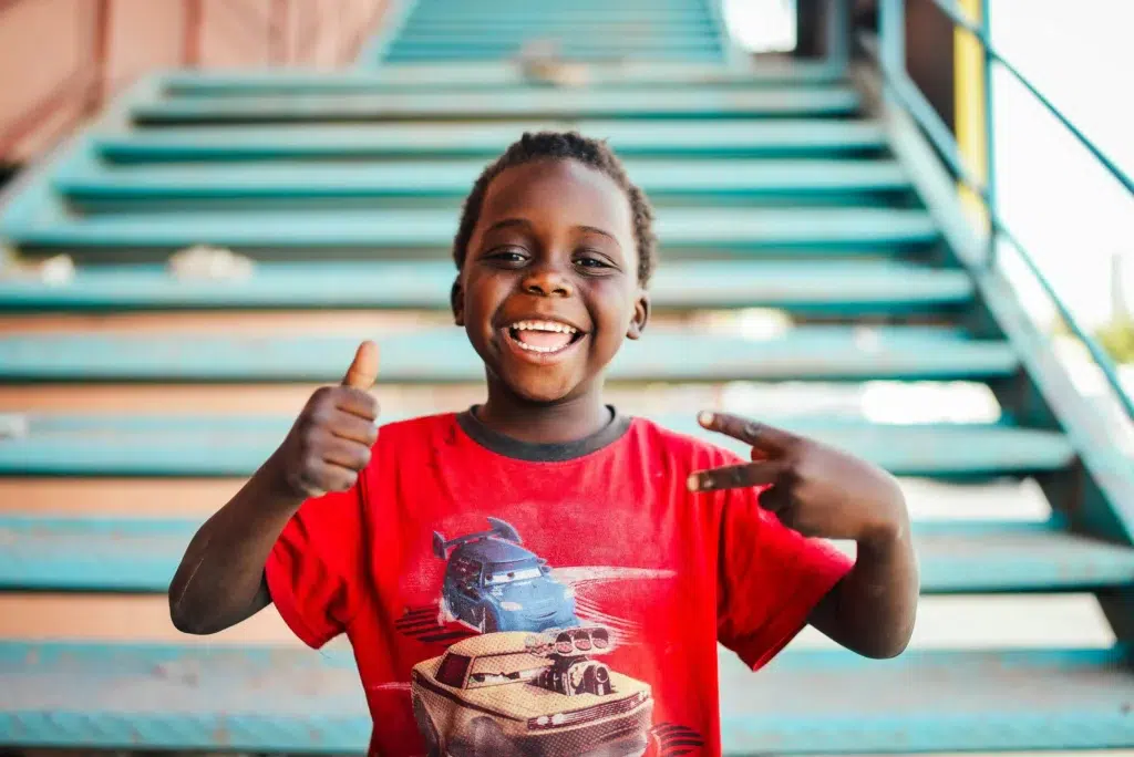 A child in a red shirt giving a thumbs up to the camera.